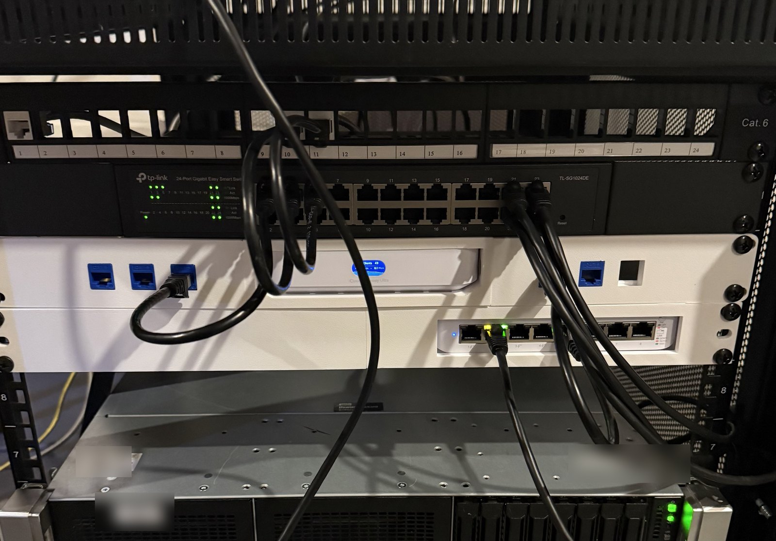 The rack: a Cat 6 patch panel, the 24-port switch, then the white 3D-printed mount holding the UniFi gateway and its small switch, with blue keystone ports on the front; a server below